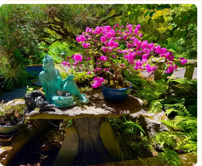 Statue with vibrant pink flowers in garden.